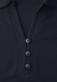 Primer plano de tela negra acanalada con tres botones negros alineados verticalmente en una prenda con escote en V.