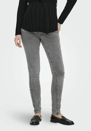 Jeans skinny grigi con una texture in denim liscia, caratterizzati da vita bassa e un classico design a cinque tasche, abbinati a mocassini neri con borchie.