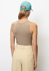 Top sin mangas color marrón combinado con pantalones amarillos claros. El conjunto presenta una textura suave y una gorra turquesa con una correa ajustable.
