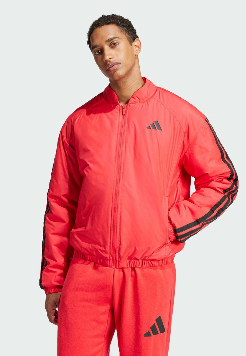 Red insulated bomber jacket with black stripes, zipper front, raised collar, and elastic cuffs. Worn with matching red pants featuring a logo.