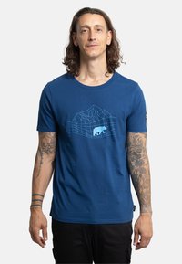 Camiseta de algodón azul con un gráfico geométrico de montaña y oso en azul claro en el pecho. Mangas cortas, cuello redondo y diseño ajustado.