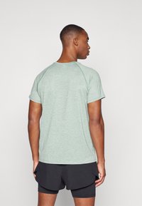 Camiseta atlética de manga corta en color verde menta con un acabado texturizado, mangas raglán y un cuello redondo, combinada con pantalones cortos negros.