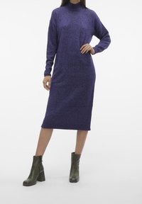 Abito a maglia viola con collo alto, maniche lunghe e una vestibilità comoda, abbinato a stivaletti a tacco verde scuro.
