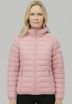 Mujer con cabello rubio claro que lleva una chaqueta acolchada rosa claro con capucha, de pie frente a un fondo gris liso.
