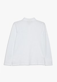 Bílá dlouhá košile s falešným límcem, zobrazená zezadu na čistém bílém pozadí.