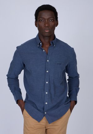 Chemise bleue à manches longues, fabriquée en tissu léger, avec une poche poitrine, des boutons blancs et une coupe décontractée.