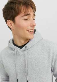Light gray hoodie with drawstrings, made of soft fabric. Features a relaxed fit and layered black shirt underneath. No noticeable patterns.
