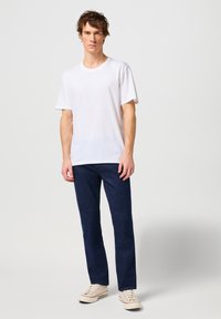 Witte katoenen t-shirt met ronde hals, gecombineerd met donkerblauwe denim jeans. Casual schoeisel in beige canvas met veters maakt de look compleet.