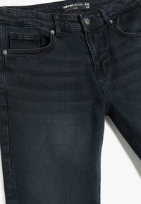 Jeans de denim ajustados de color azul oscuro, fabricados en algodón. Presentan cinco bolsillos, una cinturilla con marca y detalles en botón de metal.