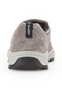 Grijze suede schoenen met een lage hak, een gestructureerd oppervlak en een zwarte treklus. Voorzien van een witte rubberen zool met een grip patroon.