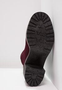 Burgunderfarbene Sneaker mit einem strukturierten Strickoberteil und einer schwarzen Gummisohle mit einem robusten Profil. "Made in Italy" auf der Sohle eingeprägt.