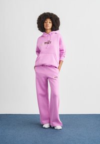 Rosa hettegenser og matchende joggebukser laget av mykt stoff, med logo foran og på siden, med en avslappet passform.