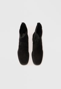 Stivaletti alla caviglia in suede nero con una texture liscia, forma affusolata e linguette sul tallone. Presentano una punta piatta e arrotondata e cuciture minime.