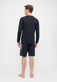 Czarna longsleeve rash guard i ciemne szorty z białymi paskami po bokach. Materiał wydaje się gładki; szorty mają kieszeń po boku.