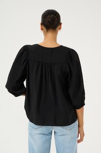 Zwarte blouse met opgeblazen mouwen en een geraffineerde achterkant. Bevat kantinzetstukken op de mouwen. Lichtgewicht stof met een zachte textuur.