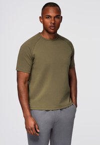 Olivenfarvet T-shirt med korte ærmer, rund hals og raglanærmer, lavet af blødt, tekstureret stof, parret med grå bukser.