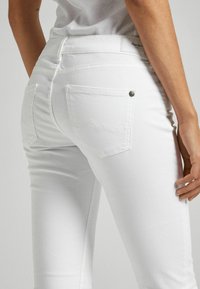 Vita jeans i denim med smal passform, featuring bakfickor och subtila sömnadsdetaljer. Tyget verkar slätt med minimal textur.