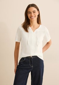 Witte korte mouwen top met een V-hals en een trekkoord. Lichtgewicht stof met een subtiele structuur, gecombineerd met donkerblauwe jeans met contrasterende stiksels.