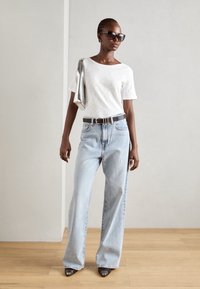 White crew neck t-shirt, light blue wide-leg jeans, black belt, black sunglasses, grey high-heeled shoes, model holding silver bag.