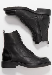 Ett par svarta läderankelstövlar med snörning, sidodragkedjor och texturerade sulor på en vit bakgrund.