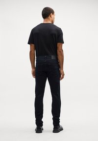 Camiseta negra ajustada y vaqueros de mezclilla oscuros. Los vaqueros presentan una textura suave, bolsillos traseros y una etiqueta de cuero negro liso en la cintura.