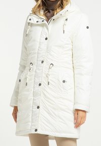 Parka blanche isolée avec capuche, dotée de cordons de serrage, de ferrures en argent, de poches latérales et d'une texture froncée sur le devant.