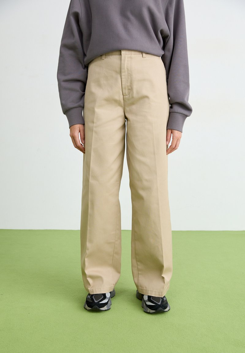 Beige leveled-hameet made of cotton, which features a smooth texture, front pleats, and a regular waistband. Combined with black sport shoes.