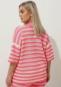 Maglione morbido di maglia oversize con strisce orizzontali rosa e crema, dettagli a occhiello e scollatura e polsini a costine. Maniche corte.