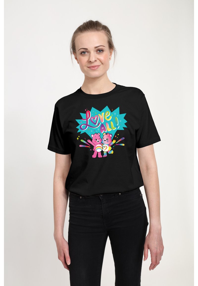 Sort t-shirt med et farverigt grafisk design, der viser to pink bjørne og teksten "Love All!" i lyse farver, sat mod en livlig blå baggrund.