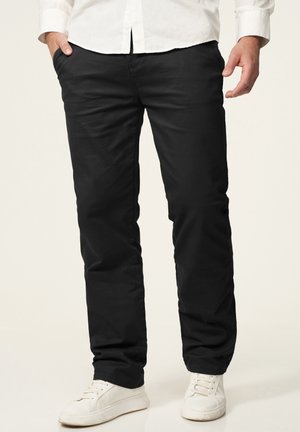 Schwarze Baumwollhose mit geradem Bein-Design, ausgestattet mit zwei Seitentaschen und einer glatten Textur, kombiniert mit weißen Sneakers.