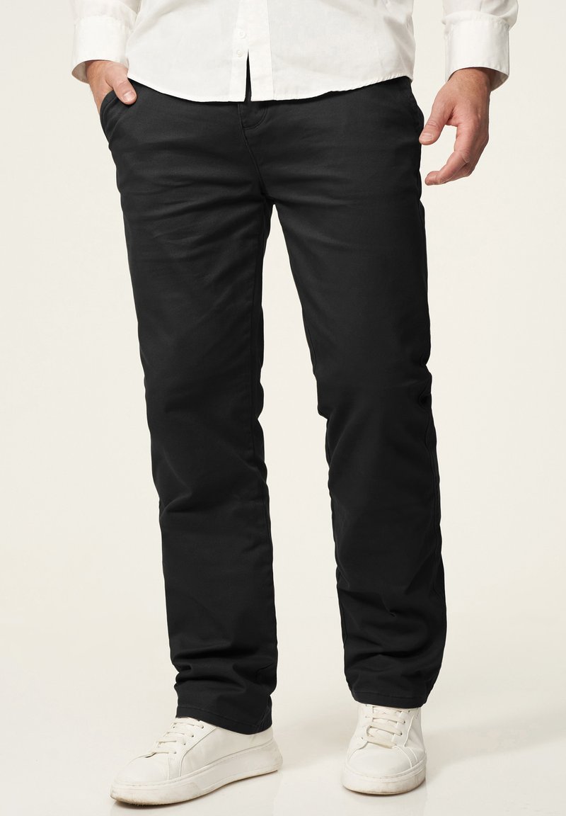 Schwarze Baumwollhose mit geradem Bein-Design, ausgestattet mit zwei Seitentaschen und einer glatten Textur, kombiniert mit weißen Sneakers.