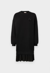 Robe sweat noire en tissu doux, avec un ourlet de jupe plissée et un détail décoratif en perles sur la poitrine. Manches longues.