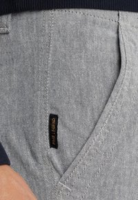 Tejido de mezclilla gris con una textura sutil, un bolsillo destacado y una etiqueta negra que dice "Pale Legend" unida cerca de la costura.