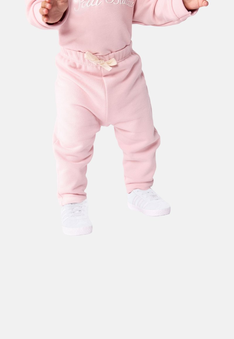 Pantaloni della tuta in pile rosa con vita elasticizzata e piccolo dettaglio a fiocco, abbinati a sneaker bianche con tre strisce.