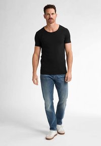 Černé tričko s krátkým rukávem z lehké látky, doplněné vybledlými modrými džínami a bílými teniskami s hnědými detaily, prezentované na modelce.