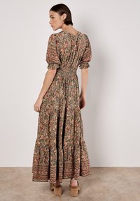 Robe maxi à motifs floraux dans des tons terreux, avec des manches bouffantes, une taille smockée et un ourlet en couches. Dotée d'un col rond et de détails subtils.
