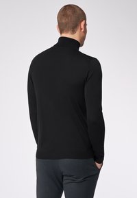 Schwarzer Rollkragenpullover mit langen Ärmeln, aus einem glatten Stoff gefertigt. Verfügt über ein figurnahes Design und einen gerippten Kragen für zusätzliche Textur.