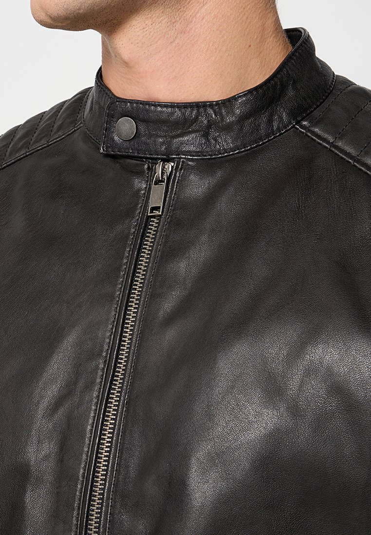 Giacca da moto in pelle nera con colletto alto, zipper visibile e dettagli testurizzati sulle spalle. Finitura liscia e design aderente.