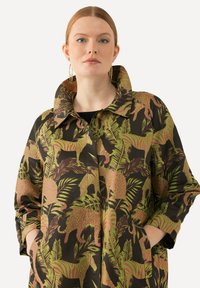 Bloemenpatroon jas met een zwarte basis en groene en roze dieren- en bladdesigns. Inclusief een puntige kraag en zijzakken.
