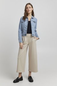 Ljusblå denimjacka med en figursydd design, två bröstfickor och silverknappar, tillsammans med beige vida byxor och svarta loafers.