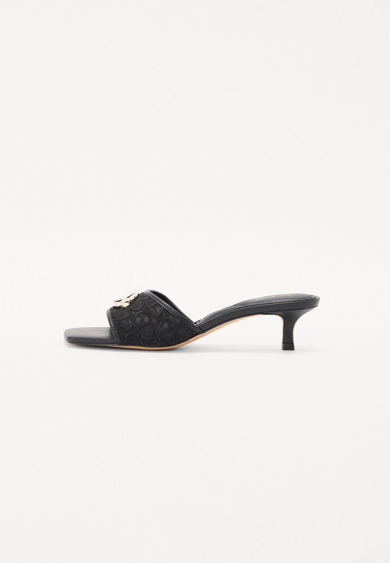 Mules noires à bout ouvert avec un dessus texturé et un petit accent métallique. Présentent un talon bas et une semelle plate. Design simple et épuré.