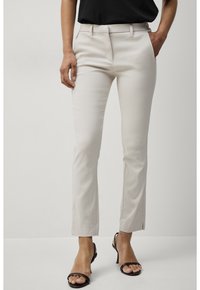 Béžové kalhoty na míru se slim fit, s bočními kapsami, poutky na opasek a jemným leskem, spárované s černými sandály na podpatku.