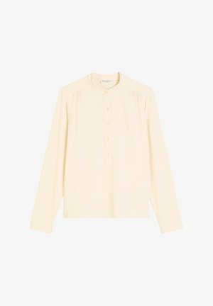 Ilgi piedurkņu, krēmkrāsas blūze ar apaļu apkakli, priekšējo pogu slīti un maziem krokām plecos. Mīksta, gluda auduma tekstūra.