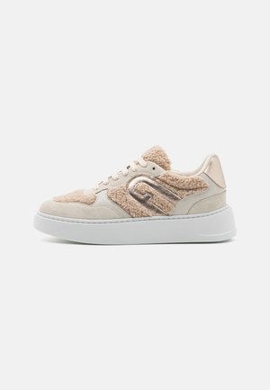 Beige en crème lage sneaker met witte dikke zool, nep-shearling stukken en metalen gouden decoratieve details aan de zijkant.