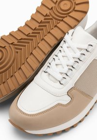 Baskets avec une tige en cuir blanc, des accents en daim tan, un panneau latéral texturé et une semelle en caoutchouc avec un motif de bande de roulement en zigzag.