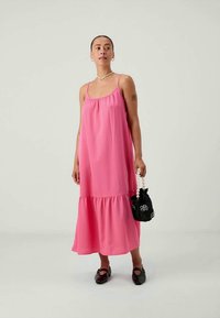 Ροζ αμάνικο φόρεμα με ραμπέ στρώσεις, φτιαγμένο από υφασμάτινη υφή. Συνδυασμένο με μαύρη τσάντα με λουλουδάτο σχέδιο και λαβή σαν μαργαρίτες.