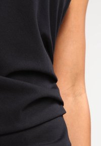 Schwarzes ärmelloses Oberteil aus einem weichen, strukturierten Stoff, mit gerafften Details an der Seite für zusätzliche Dimension und Form.