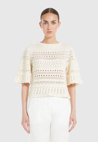 Un haut en tricot crème avec des manches courtes évasées, présentant un motif texturé avec des mailles ouvertes et un ourlet festonné.
