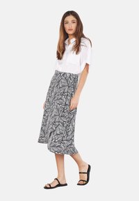 Blusa blanca de manga corta con botones, combinada con una falda midi de patrón de hojas en blanco y negro. La modelo lleva sandalias negras.