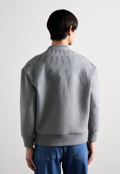 Grå sweatshirt med ett texturerat blixtmönster i en mörkare grå nyans på baksidan. Har ribbad krage och mudd, avslappnad passform.
